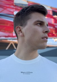 Λευκό βαμβακερό T-shirt με στρογγυλή λαιμόκοψη και κοντά μανίκια, που διαθέτει μαύρο κείμενο "Marc O'Polo EST. IN STOCKHOLM" μπροστά.