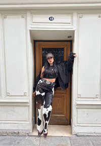 Sort bomberjakke, sort crop top og bukser med ko-print og knapper. Mørkebrun og hvidt mønster; spidse hæle. Trædør med nummer 48.