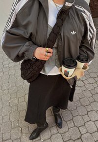 Hallid hall sportlik jakk valgete triipudega, must punutud kott, hall nööbiga särk, must poolpikk seelik ja kõrge mustad saapad. Hoitakse kahte kohvitass. 