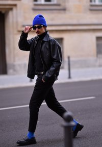 Μαύρο δερμάτινο μπουφάν, μαύρο πουλόβερ, μαύρο παντελόνι, μπλε σκουφάκι, γυαλιά ηλίου, μπλε κάλτσες και μαύρες λουστρίνι; αστική σκηνή.