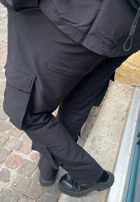 Svarta cargo byxor med sidofickor, gjorda av ett mjukt tyg. Kombinerade med svarta stövlar med tjocka sålar, mot en kullerstensyta.