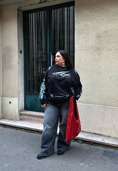 Sudadera gráfica negra de manga larga con diseños en blanco y azul, combinada con jeans de pierna ancha grises y un bolso tote rojo brillante. Zapatos negros.