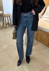 Ψηλόμεσα μπλε τζιν παντελόνια με ευθύ κομμάτι, συνδυασμένα με μαύρο σακάκι και μαύρες γόβες με尖尖尖尖尖尖尖尖尖尖角. Λεπτομερές μικρό τσαντάκι.