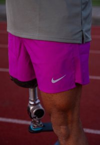 Nike ytelsesshorts i levende rosa, med en sølvlogo. Vist sammen med et protese-ben, plassert foran en rød løpebane.