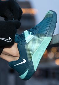 Nike sportcipő türkiz és menta színátmenettel, hálós felsőrésszel, jellegzetes gumitalppal és kiemelkedő fehér Swoosh logóval.