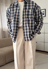 Hedvábná košile s dlouhým rukávem, károvaná v námořnické modré a krémové barvě, s knoflíkovým zapínáním. Doladěná s béžovými širokými kalhotami a hnědým opaskem.