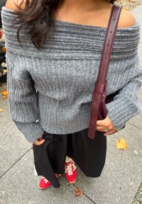 Grå ribbet av-shoulder genser med lange ermer, sammen med et svart skjørt. Burgunderrød håndveske med en sleek stropp og røde joggesko.