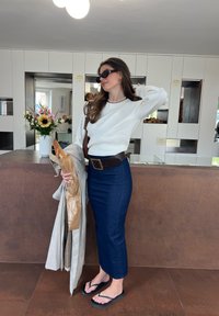 Bela dolga majica s sleeves, temno denim svinčnik krilo, rjava pas, japonke, drži baget in svetlo barvo trench plašč.