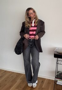 Blazer oversize à carreaux marron, polo rose à rayures, jean gris, sac noir et baskets argentées. Textures lisses et coupe décontractée.