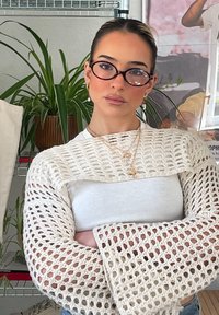 Sweater branco de malha com design rendado e mangas largas, combinado com um top branco justinho. Acessoriado com colares dourados em camadas.