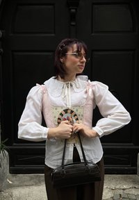 Blusa bianca con maniche a palloncino, un gilet rosa ricamato con un gatto e una piccola borsa nera con stampa coccodrillo.