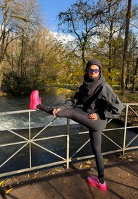 Must must, soonikud mustad retuusid ja erkroosa spordijalatsid. Modell poseerib restil, taustal jõeäärne mets.