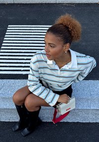 Stripete langermet skjorte med blå, brune og hvite striper, kombinert med et svart skjørt og knelange svarte støvler. Tilbehør inkluderer en liten hvit håndveske.