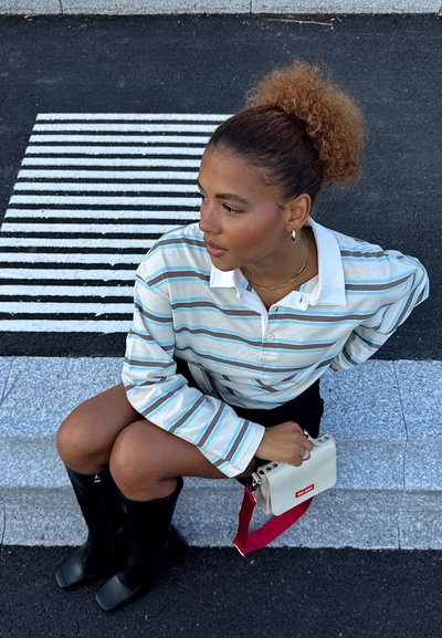 Camisa de manga larga a rayas con líneas azules, marrones y blancas, combinada con una falda negra y botas negras hasta la rodilla. Los accesorios incluyen un bolso pequeño blanco.