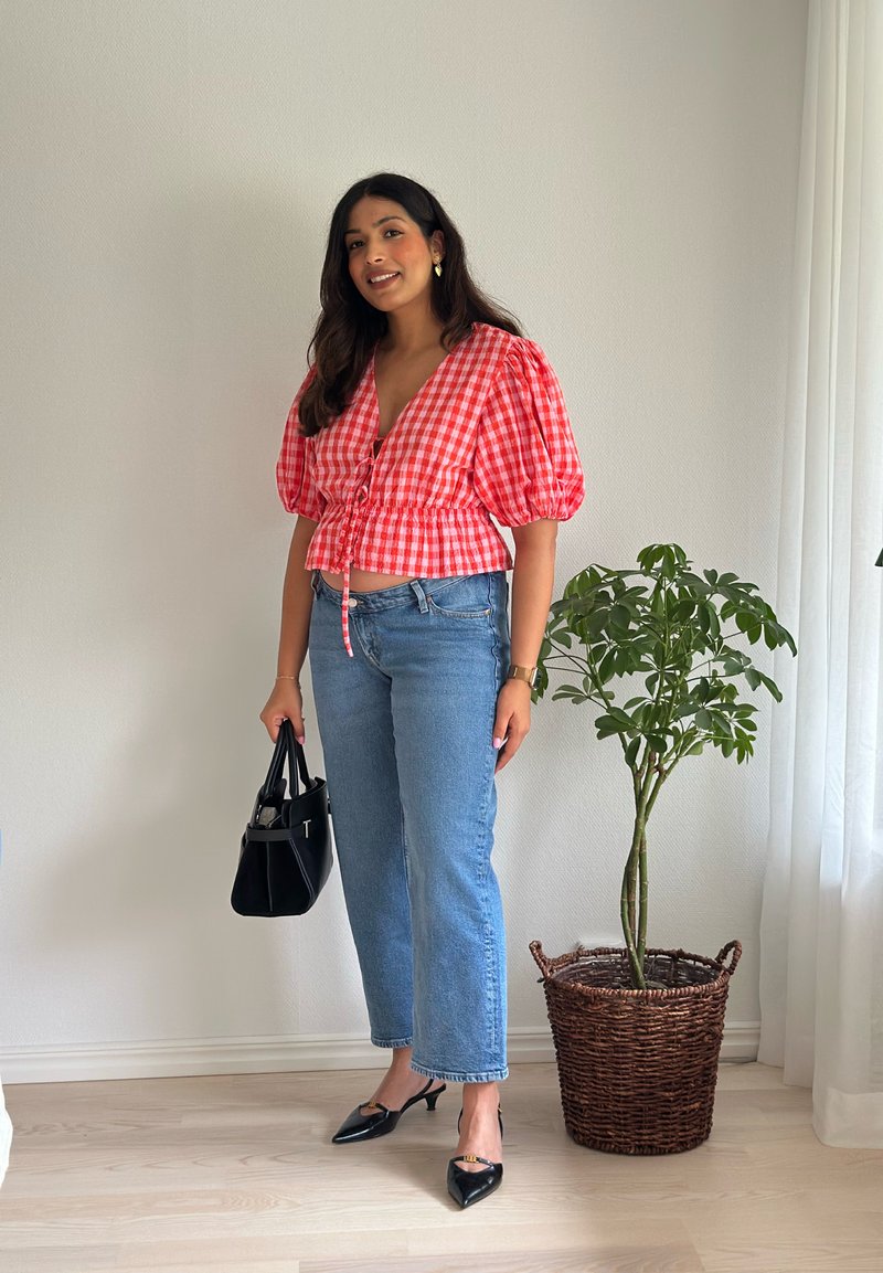 Blusa cropped em gingham vermelho e branco com mangas bufantes, combinada com jeans de perna reta azul claro e sapatos de salto fino pretos, segurando uma bolsa preta.