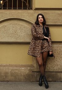 Kabát s leopardím vzorom a golierom, v kombinácii s čiernym topom a minisukňou. Čierne členkové čižmy. Hladká textura na textúrovanom pozadí.