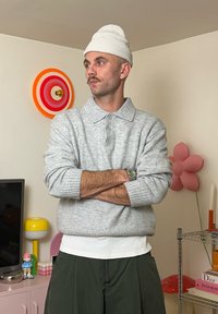 Helehall kootud kampsun kraega, valge aluskiht ja tumerohelised lühikesed püksid. Tarvikute hulka kuuluvad valge müts ja kell.