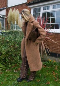 Brown furry coat with an oversized collar, paired with leopard print wide-leg trousers. A brown handbag and dark shoes complete the outfit.