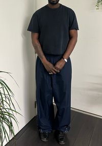 Pantalon bleu marine, coupe ample, avec taille élastique et bandes latérales ; accompagné d'un t-shirt noir à manches courtes et de chaussures noires.