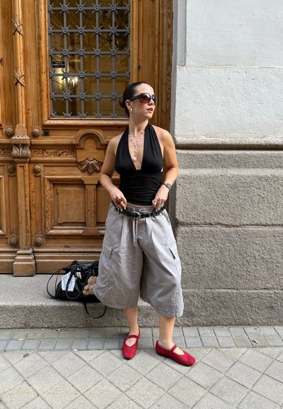 Top halter negro, culottes de lino gris con bolsillos, zapatos rojos de deslizamiento, joyería de plata y un bolso negro con un llavero de peluche.