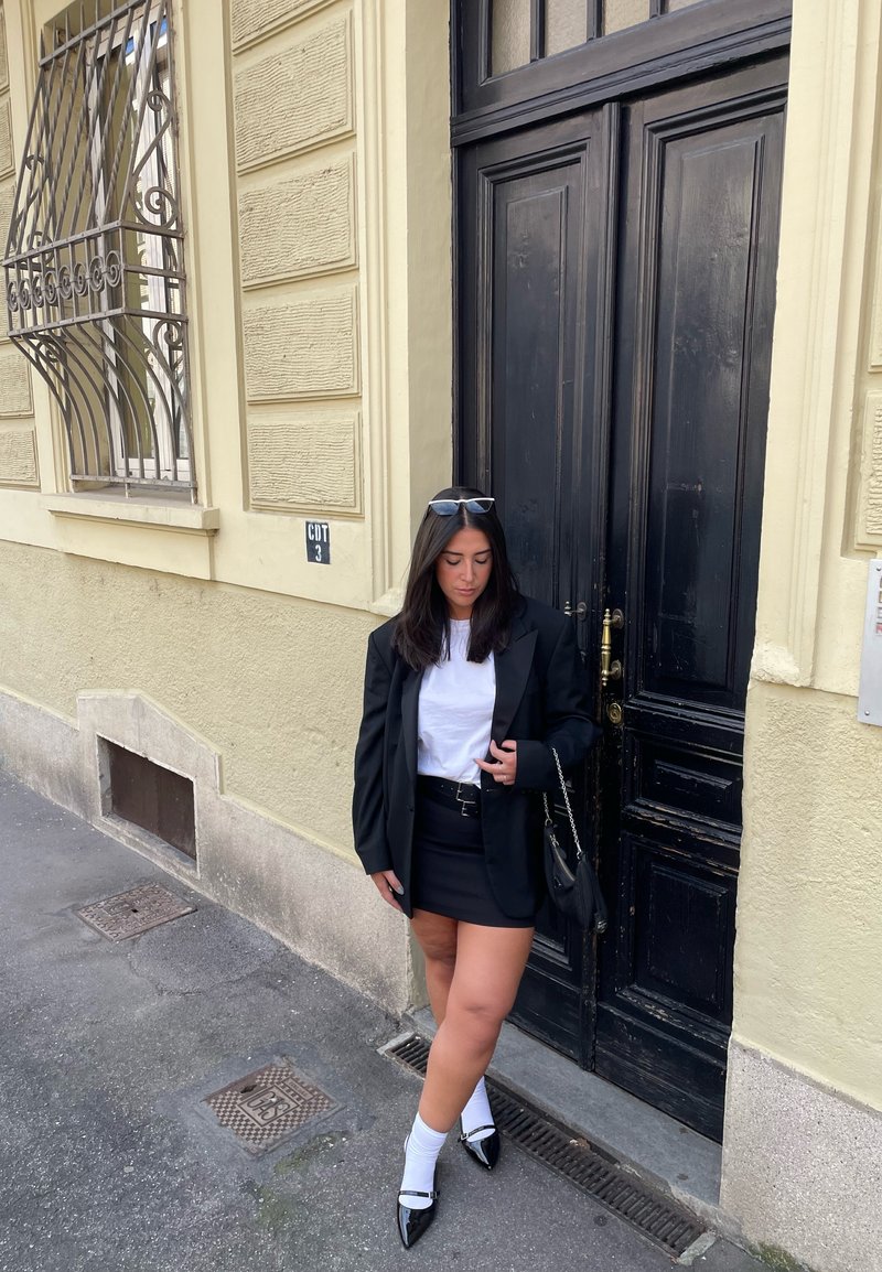 Μαύρο oversized σακάκι πάνω από λευκό t-shirt, σε συνδυασμό με μαύρη μίνι φούστα. Μαύρα παπούτσια από πατίνα και λευκές κάλτσες ολοκληρώνουν το look. Μαύρη τσάντα.