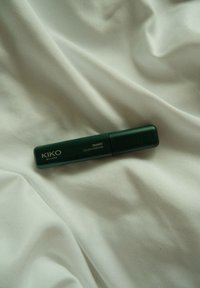 Σκούρο πράσινο σωληνάριο μάσκαρας με ματ φινίρισμα και στρογγυλές άκρες, με την επιγραφή "KIKO MILANO SMART COLOUR MASCARA" σε λευκή γραμματοσειρά, resting πάνω σε ανοιχτόχρωμο ύφασμα.