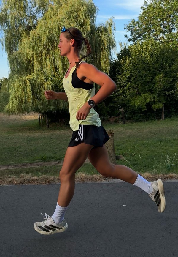 Mujer con ropa deportiva corriendo por un camino pavimentado con árboles y césped al fondo durante el día.