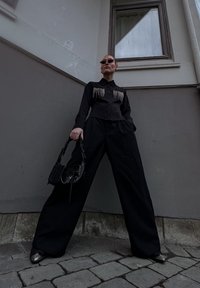 Mustat lyhyet paidat, joissa on fringed yksityiskohtia, leveät mustat housut ja teräväkärkiset hopeasomisteiset kengät. Mukanansa pieni musta käsilaukku.