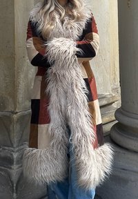 Lappet frakk med varierte farger: brun, beige og rød. Myk, lang faux fur kant og mansjetter, i kontrast til det glatte stoffet på kroppen.