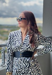 Blazer a strisce zebra in bianco e nero con una larga cintura nera dotata di doppia fibbia dorata. Abbinato a occhiali da sole rotondi neri e capelli lunghi e mossi.