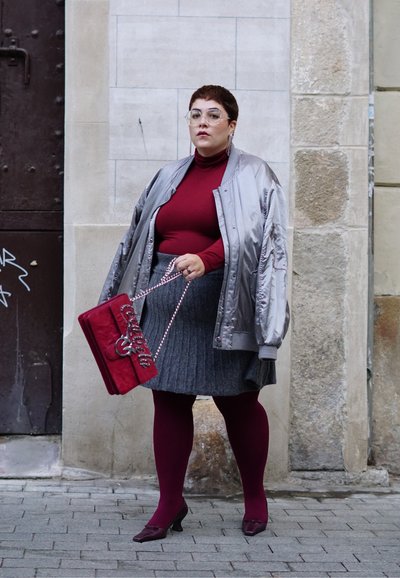Chaqueta bomber plateada, suéter de cuello alto burdeos, falda gris con pliegues, medias burdeos, bolso rojo con cadena y tacones oscuros.