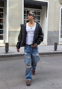 Črna puhasta jakna z ovratnikom iz krzna, beli top, oprijete modre raztrgane kavbojke in rjavi čevlji. Kapa z vzorcem za kamuflažo, srebrna verižica.