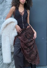 Musta hihaton toppi vetoketjulla, kerroksellinen ruskea pitsihame kukkakuviolla, yhdistetty valkoiseen tekoturkistakkiin. Tumma tausta.