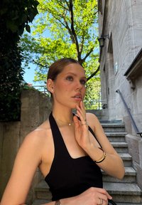 Vestido negro sin mangas con un diseño ajustado; la modelo lleva un collar con un pequeño colgante y múltiples anillos en los dedos; fondo de una escalera de piedra.