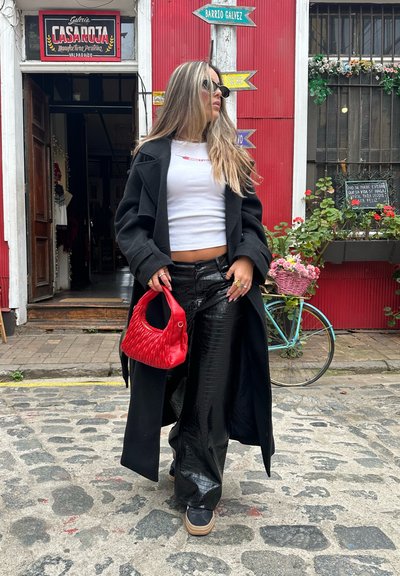 Abrigo largo negro, top corto blanco, pantalones negros brillantes con textura de cocodrilo y un bolso tejido rojo. Zapatillas con plataforma color canela.