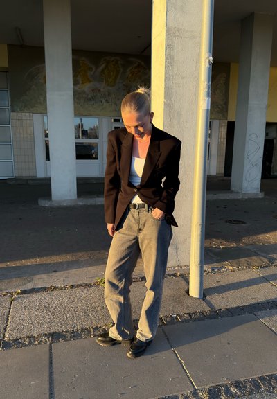 Blazer negro, top blanco de tirantes, jeans de pierna ancha grises y zapatos de plataforma negros; las texturas varían entre suaves y resistentes; luz solar suave.