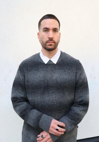 Pull gris en tricot avec un col côtelé, des rayures horizontales décolor ées et des manches longues. Les accessoires comprennent plusieurs bagues en argent.