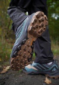 Trail schoenen met een gestructureerde bruine zool, een zwart en teal bovenwerk, en opvallende noppen voor grip. Continental branding zichtbaar op de zool.