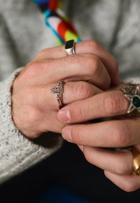 Mains portant plusieurs bagues en argent, dont une avec un dessin d'orbe et de croix, tenant un objet coloré à motifs.