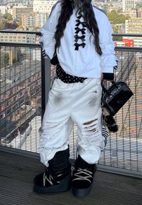 White zip-up jacket featuring black bow accents, a black and white polka dot belt, distressed white trousers, and chunky black boots. Accompanied by a black handbag.