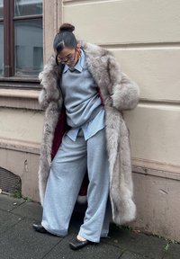 Sivý kožušinový kabát s červenou podšívkou, nosený cez svetlosivý top a široké sivé nohavice. Čierne baleríny dopĺňajú outfit, ktorý má uvoľnený strih.