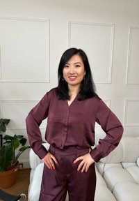 Blouse en satin bordeaux à manches longues et fermeture à boutons, associée à un pantalon taille haute assorti en texture lisse.