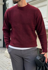 Bordowy sweter z dzianiny z ribbowym okrągłym dekoltem, w połączeniu z szarymi spodniami. Miękka faktura, lekko luźny krój i długie rękawy.