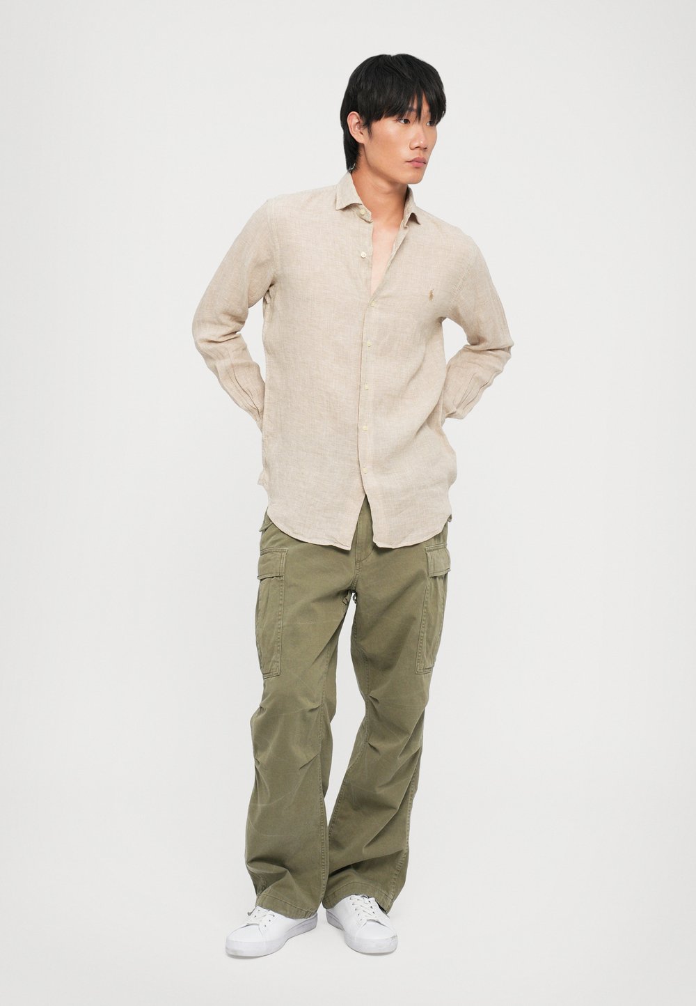 Camisa de lino beige claro con botón frontal y cuello, combinada con pantalones cargo verde oliva que cuentan con múltiples bolsillos y un corte relajado.