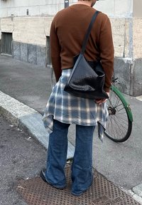 Καφέ ριγέ μπλούζα με μακρύ μανίκι, γαλάζιο καρό φούτερ δεμένο στη μέση, γαλάζια νάυλον τζιν, μαύρη πλεκτή τσάντα ώμου, στέκεται σε επιφάνεια από τσιμέντο.