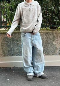 Pull gris clair en maille avec un col, associé à un jean bleu clair ample et des sabots gris. Look simple et décontracté.
