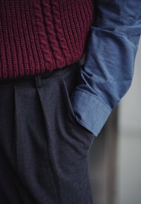 Pull en tricot bordeaux avec un motif torsadé, associé à une chemise à col bleu clair et un pantalon sombre avec un devant plissé.