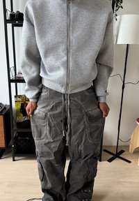 Sweat-shirt zippé gris avec un col montant, associé à un pantalon cargo gris ample et texturé, doté de multiples poches et d'une taille à cordon de serrage.