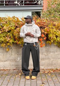 Puffer bunda v sivom maskáčovom vzore, čierne široké nohavice a svetlohnedá obuv. Doplnky zahŕňajú retiazky a visacie prívesky.