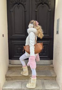 Fehér dzseki műszőrme gallérral, rózsaszín bolyhos kesztyűk, barna kézitáska, fehér leggings és krémszínű hócsizma kőlépcsőkön.